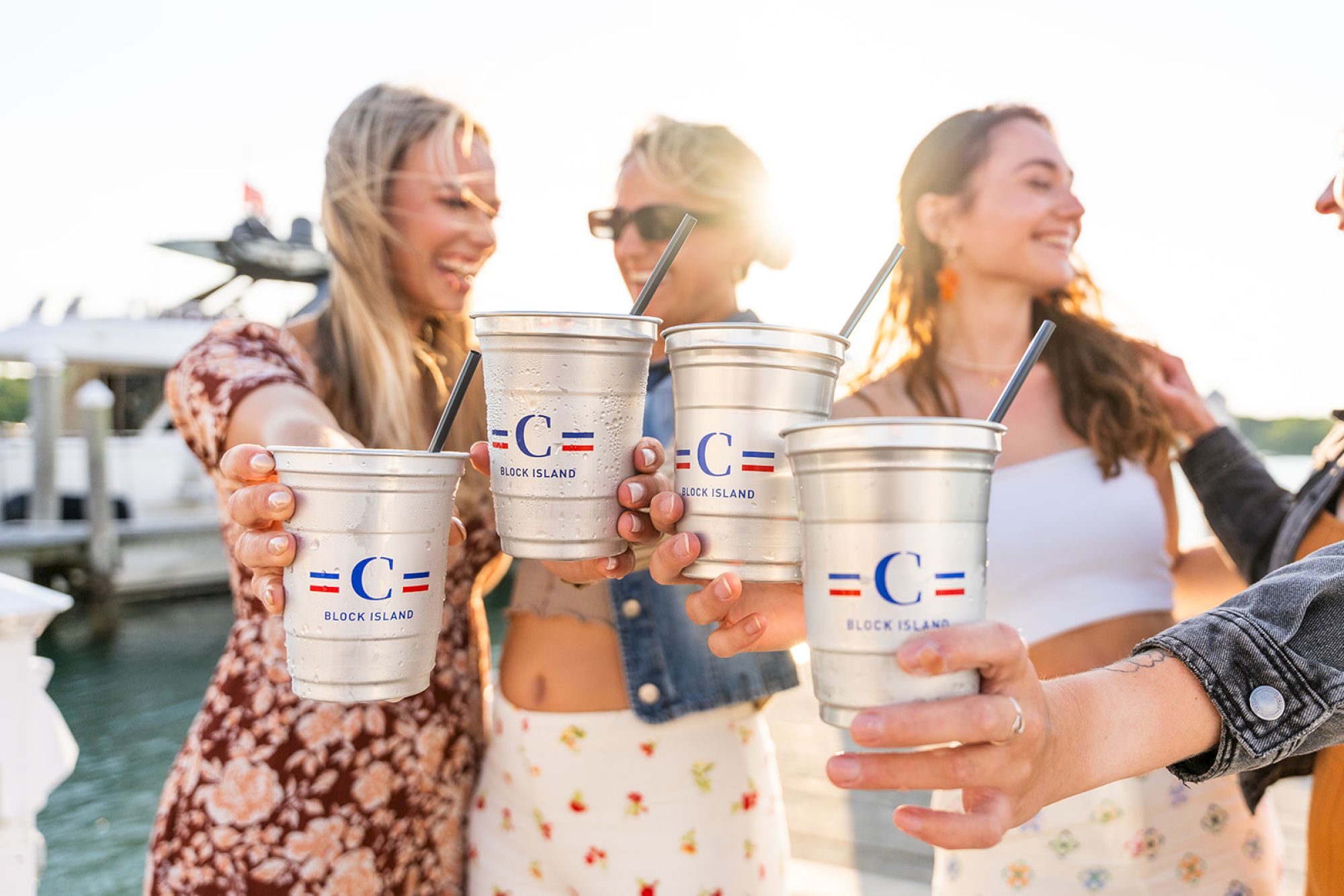 A group of people are raising metal cups with straws, branded with 